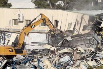 Una excavadora CAT amarilla demolió un edificio en Jerusalén Oriental, sede de la UNRWA, creando una pila de escombros y escombros.