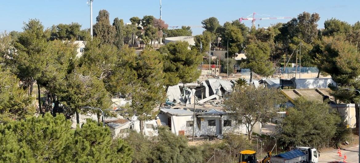 Aerial view of the UNRWA headquarters in East Jerusalem undergoing demolition, with damaged buildings, construction equipment, and surrounding trees visible.