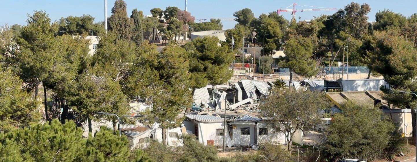 Une vue aérienne du siège de l'UNRWA à Jérusalem-Est en démolition, avec des bâtiments endommagés, des équipements de construction et des arbres environnants visibles.