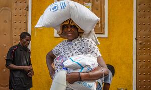 A woman in Haiti carries a WFP food sack and a milk container after receiving emergency food aid in Port-au-Prince, Delmas 31, under challenging conditions.