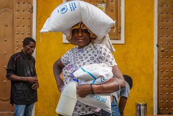 Une femme haïtienne porte un sac de nourriture du PAM et un conteneur de lait après avoir reçu une aide alimentaire d'urgence à Port-au-Prince, Delmas 31, dans des conditions difficiles.