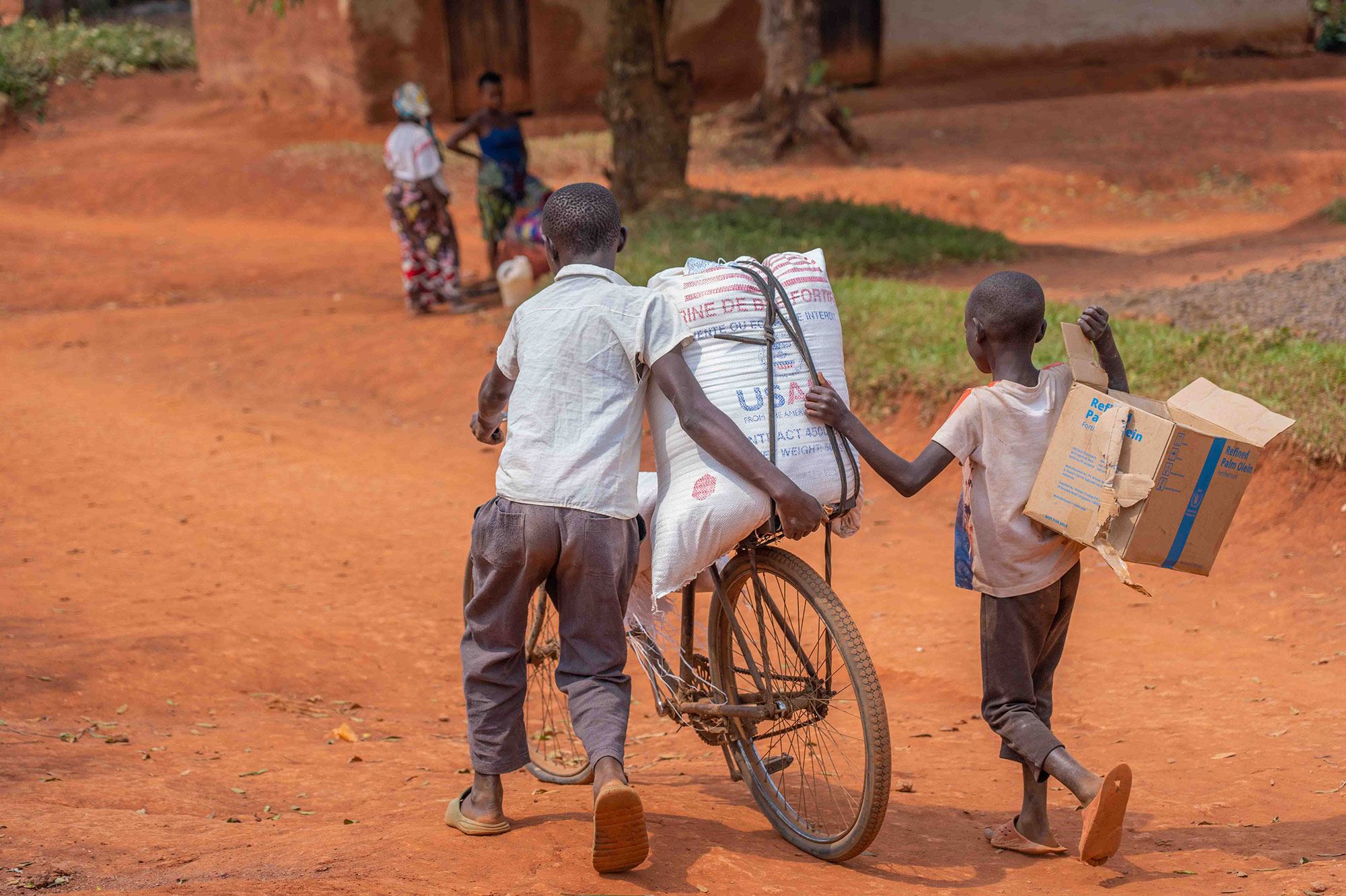 Deux jeunes garçons transportent de l'aide alimentaire à vélo à Beni, au Nord-Kivu, en RDC.