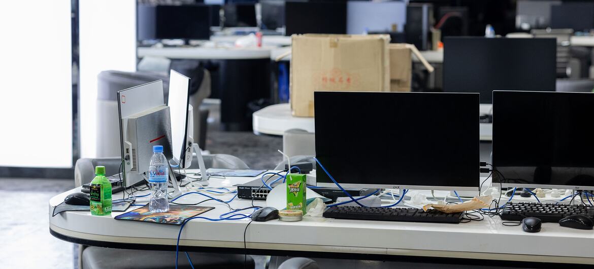 Un espace de bureau vide avec plusieurs écrans informatiques, claviers et boissons sur des bureaux, ce qui indique un centre d'escroquerie perquisitionné au Cambodge.