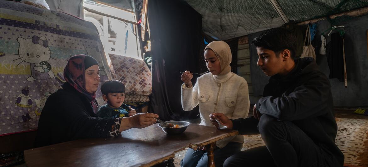 Une famille palestinienne se rassemble autour d'une petite table en bois dans un refuge de fortune pour rompre leur jeûne pendant le Ramadan, en s'appuyant sur des repas chauds fournis par la communauté comme seule source de nourriture cuite.