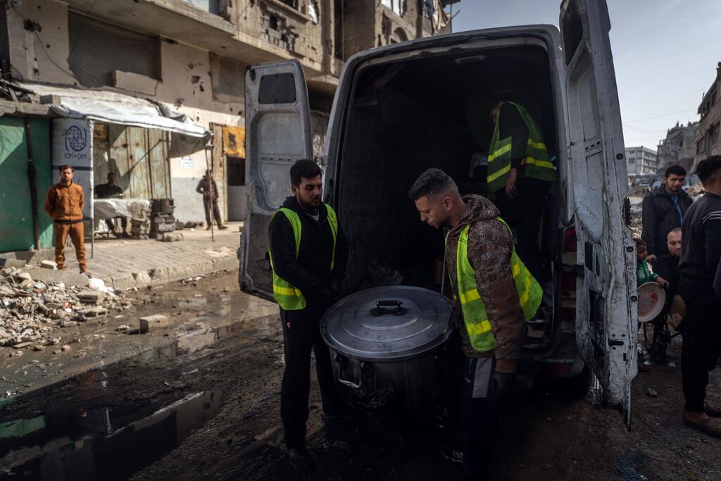 متطوعان ينزلان قدرا كبيرا من الطعام من شاحنة صغيرة في غزة.