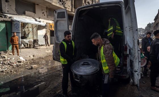 متطوعان ينزلان قدرا كبيرا من الطعام من شاحنة صغيرة في غزة.
