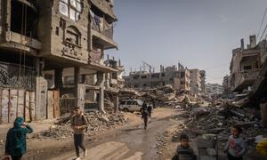 بچے اور بالغ رمضان کے دوران غزہ میں رمضان کے دوران ایک تباہ شدہ گلی سے گزرتے ہیں، جہاں خاندان کھنڈرات اور تباہ شدہ عمارتوں کے درمیان کمیونٹی باورچی خانوں کی طرف سے فراہم کردہ افطار کھانے کے لیے جمع ہوتے ہیں۔