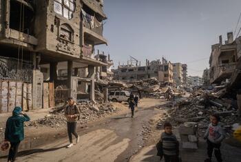 Des enfants et des adultes marchent dans une rue détruite à Gaza pendant le Ramadan, où les familles se rassemblent pour des repas d'Iftar fournis par les cuisines communautaires au milieu des décombres et des bâtiments endommagés.