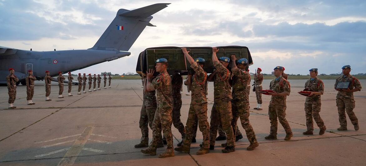Des soldats de la FINUL portent un cercueil sur un aérodrome, avec une ligne d'autres soldats rendant les honneurs en arrière-plan, près d'un avion de transport militaire.