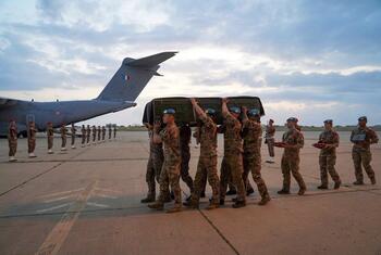 Des soldats de la FINUL portent un cercueil sur un aérodrome, avec une ligne d'autres soldats rendant les honneurs en arrière-plan, près d'un avion de transport militaire.