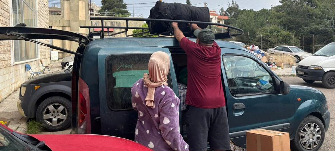 A WHO team member helps a displaced family load belongings onto a vehicle roof rack at a shelter in Chhim, Lebanon, as they prepare to return home following a ceasefire.