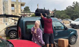 A WHO team member helps a displaced family load belongings onto a vehicle roof rack at a shelter in Chhim, Lebanon, as they prepare to return home following a ceasefire.