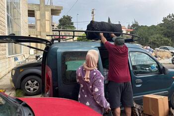 A WHO team member helps a displaced family load belongings onto a vehicle roof rack at a shelter in Chhim, Lebanon, as they prepare to return home following a ceasefire.