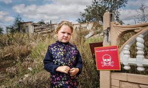 Veronika, 4, stands near a sign that reads "Danger of Mines". Chistovodivka, Kharkiv region, Ukraine (file, May 2025)