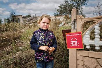 Veronika, 4, stands near a sign that reads "Danger of Mines". Chistovodivka, Kharkiv region, Ukraine (file, May 2025)
