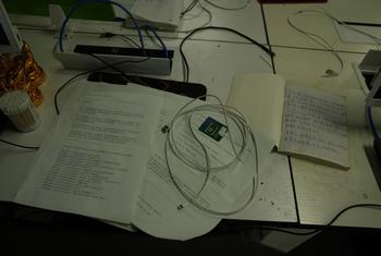 A desk with papers, a SIM card in a tray, a coiled USB cable, and a handwritten notebook.