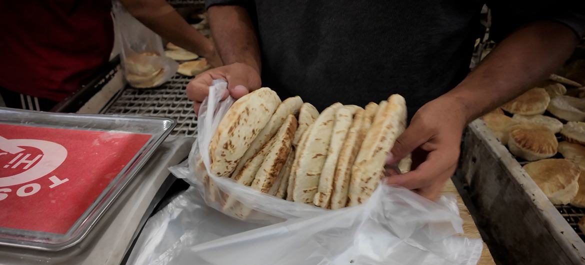 Une personne tient un sac en plastique rempli de pain pita dans une boulangerie de Gaza.