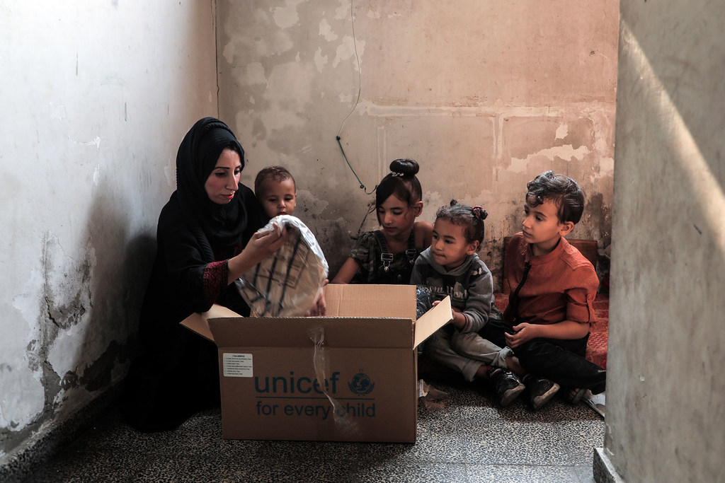 Una madre y sus hijos observan un kit de ropa de invierno procedente de una caja de UNICEF.
