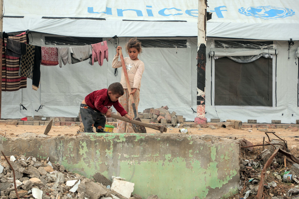 两名儿童在加沙城一顶帐篷外清理瓦砾。