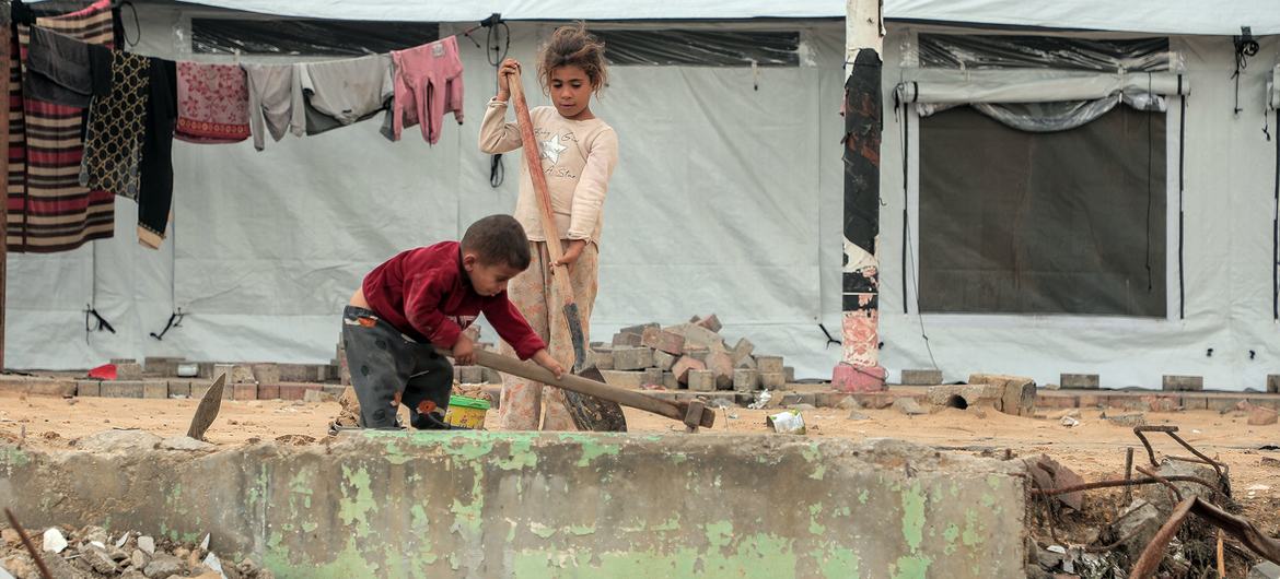 Two children clear debris outside a tent in Gaza City. 