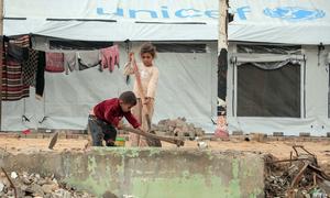 Two children clear debris outside a tent in Gaza City. 
