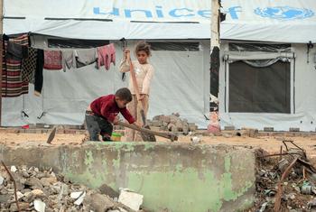 Two children clear debris outside a tent in Gaza City. 