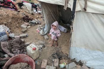 Un enfant palestinien se tient devant une tente de fortune à Gaza, au milieu des décombres.