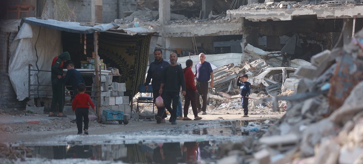  UN News People walk through a destroyed neighbourhood of Gaza City.
