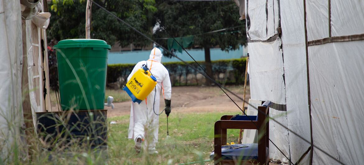 A hygienist in a white protective suit and yellow backpack sprayer disinfects a tent at a hospital in Bunia, Democratic Republic of the Congo.