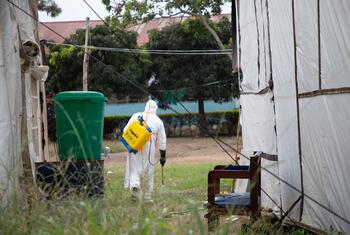 A hygienist in a white protective suit and yellow backpack sprayer disinfects a tent at a hospital in Bunia, Democratic Republic of the Congo.