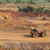Un gros camion jaune transporte des matériaux sur un chemin de terre d'un site minier de nickel, avec d'autres équipements miniers et de la terre excavée visibles en arrière-plan.
