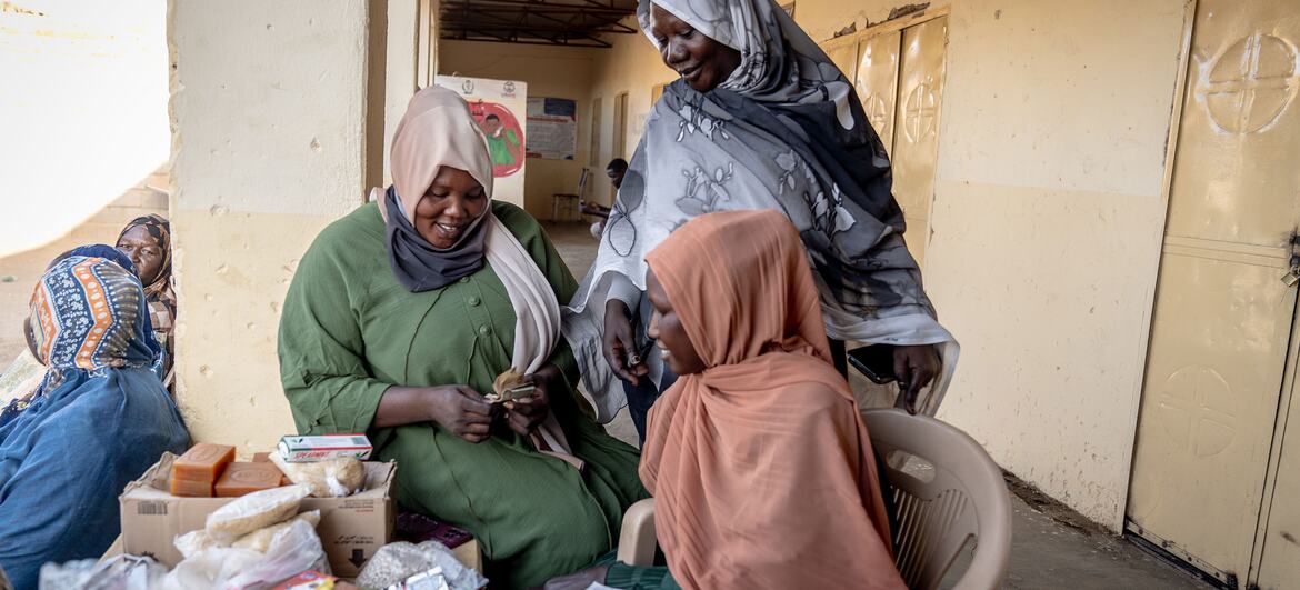 Local women gather at a VSLA meeting in Kadugli, KSS, under a covered walkway of a building.