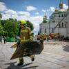 Um bombeiro ucraniano carrega um grande pedaço de entulho em frente ao Mosteiro das Cavernas de Kiev (Kyiv Pechersk Lavra), com outros membros da equipe de emergência e um caminhão de bombeiros visíveis ao fundo.