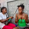 Deux femmes sont assises contre un mur en béton, en train de tresser des cheveux.