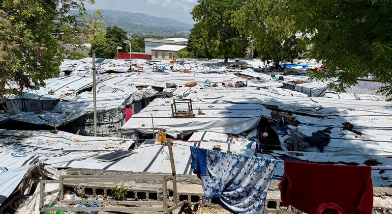 Un camp de réfugiés en Haïti, avec des abris de fortune faits de bâches, et des montagnes visibles en arrière-plan.