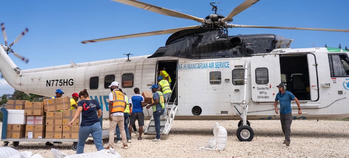 A group of people load medical supplies onto a white World Food Programme helicopter, operated by CHI Aviation, at an airfield in Haiti.