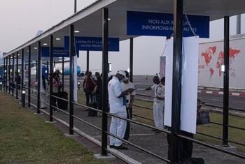 Health workers in white uniforms and masks screen travelers at an airport terminal in the Democratic Republic of Congo during the Ebola outbreak.