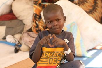 A young Sudanese refugee boy in Chad makes a heart shape with his hands, wearing a UNICEF wristband.