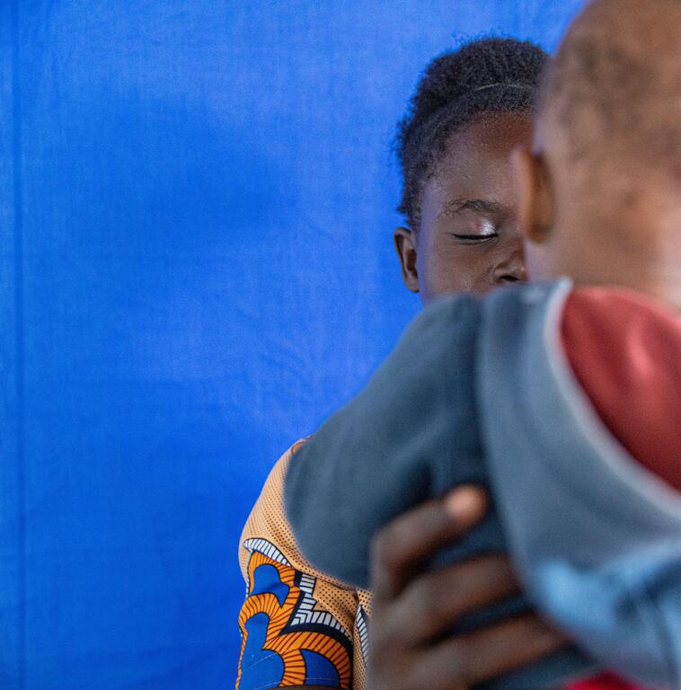 An African woman holds a child in her arms against a blue background.