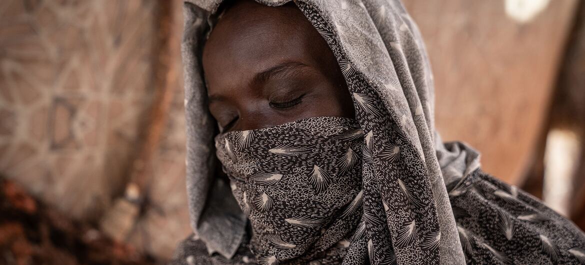 A Sudanese woman wearing a patterned headscarf sits inside a tent in a displacement camp in North Darfur.
