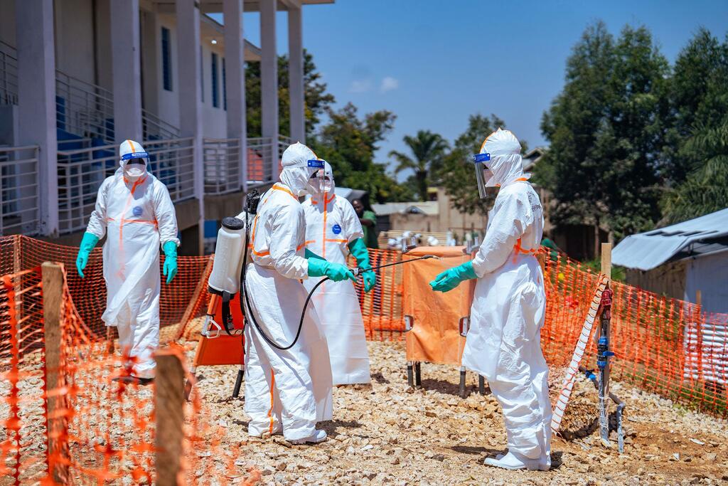 Des agents de santé entièrement équipés de protections désinfectent un site à l'aide d'un pulvérisateur lors d'une intervention de l'OMS face à une épidémie d'Ebola en République démocratique du Congo.