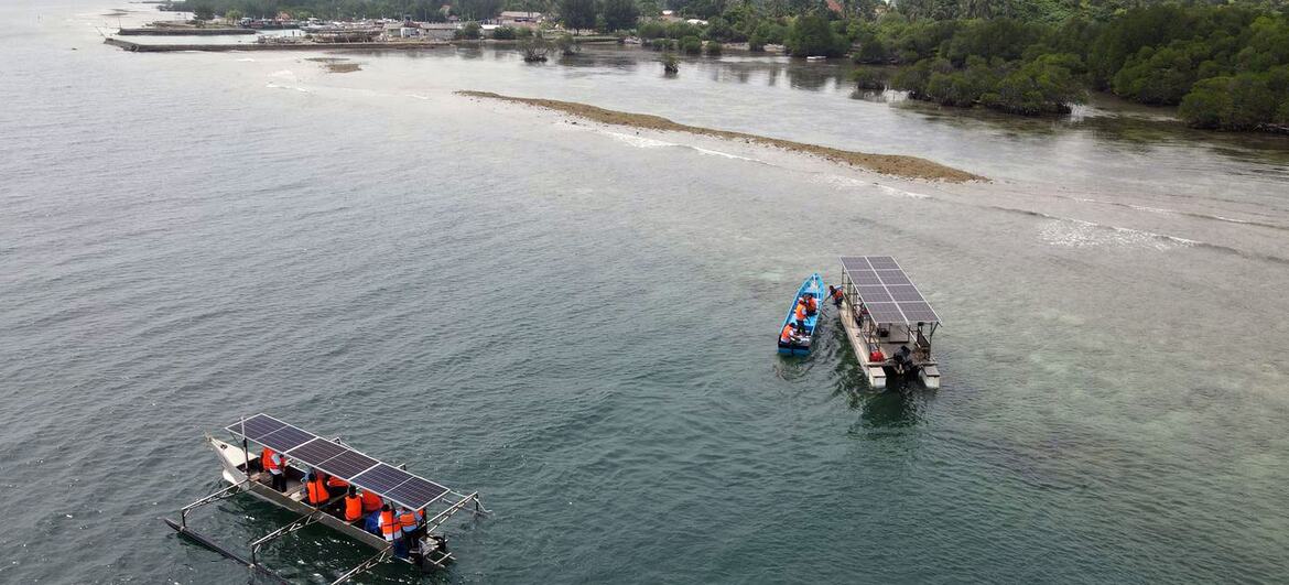 Aerial view of two solar-powered boats on the water near a coastal village in Indonesia.