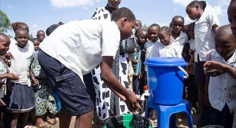Un estudiante se lava las manos en un dispensador de agua mientras otros estudiantes y adultos observan durante una sesión de educación sobre higiene en una escuela de Bunia, República Democrática del Congo.