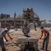 Three men work with a piece of metal on a makeshift concrete table amidst the rubble of a destroyed building in Gaza.