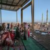 IDP settlement in Gedaref, Sudan, showing displaced people in a former bus station, with a mosque in the background.