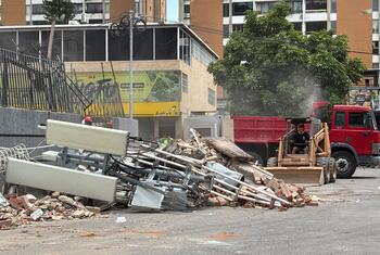 Rubble and debris from a collapsed building in Venezuela, with a backhoe and dump truck clearing the site.