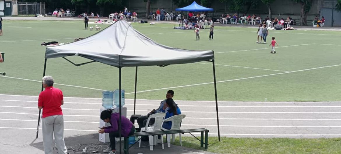Pessoas se reuniram sob uma tenda e em uma pista de atletismo em um complexo esportivo ao ar livre.
