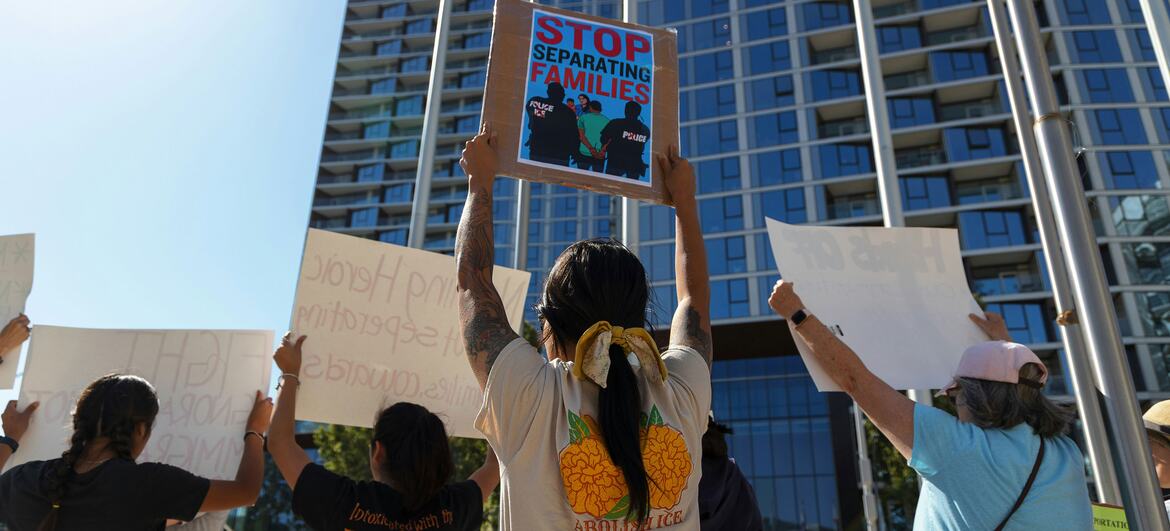 A group of people protest, holding signs in front of a modern building.