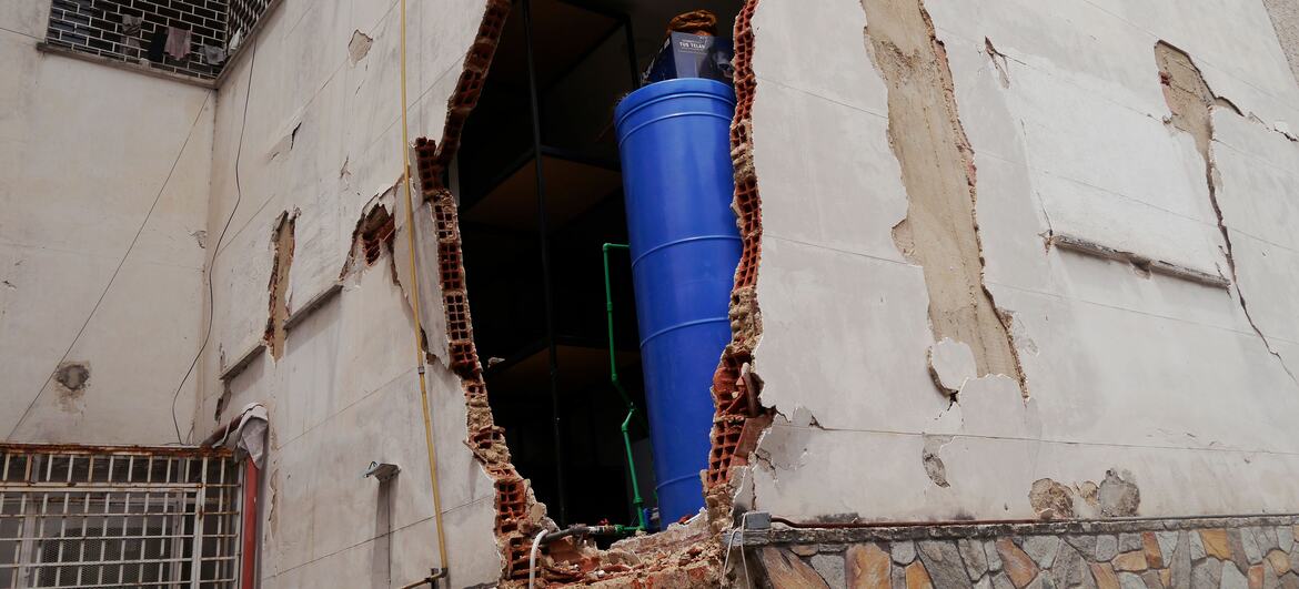 Damaged building in Caracas, Venezuela, showing a large hole in the wall with exposed brick and a blue barrel inside.