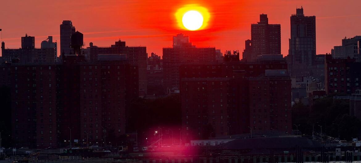Pôr do sol sobre o horizonte da cidade com um corpo d'água em primeiro plano.